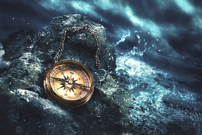 The Pirate's Code. An image of a compass on a boulder, with a stormy, evening sea in the background.